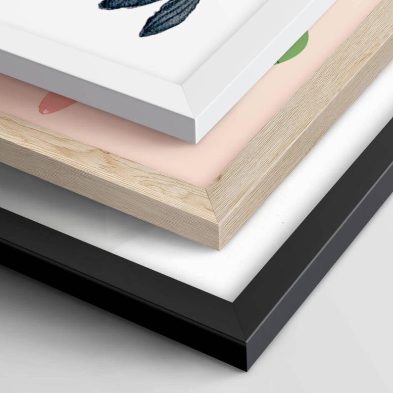 Close-up view of three different frame options: a white frame, a natural wood frame, and a black frame. The image shows the corner details of each frame, highlighting their distinct textures and finishes for displaying artwork.