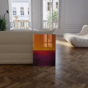 May include: An abstract art print featuring a gradient of colors. The top half transitions from orange to yellow, while the bottom half is a deep purple. The artwork is displayed in a modern living room setting.