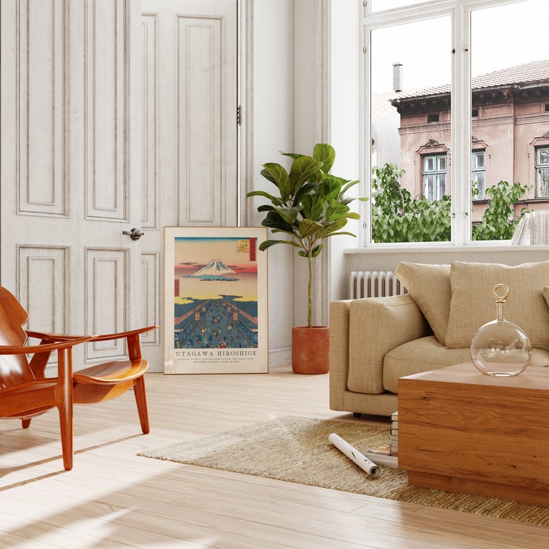 May include: A living room interior with a wooden coffee table, a beige sofa, a brown armchair, a potted plant, and a framed print of a Japanese landscape with the text "UTAGAGAWA HIROSHIGE".