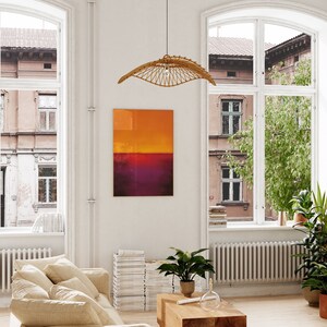 May include: A living room with large windows, a beige sofa, and a wooden coffee table. A woven rattan pendant light hangs from the ceiling. An abstract painting with orange and purple hues is on the wall. Potted plants add greenery.