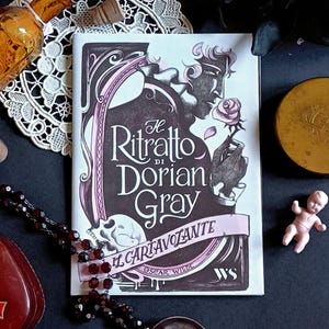 Może przedstawiać: Zbiór przedmiotów w stylu vintage, w tym książka zatytułowana "Il Ritratto di Dorian Gray", mały zegar, szklana karafka, naszyjnik z koralików i etui na karty do gry. Przedmioty są ułożone na ciemnej powierzchni, tworząc gotycką estetykę.