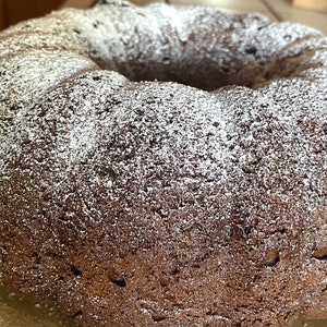May include: A close-up of a chocolate bundt cake dusted with powdered sugar. The cake has a rich brown color and a slightly textured surface.