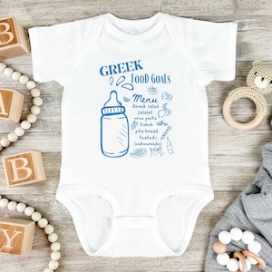 Op de afbeelding: Witte baby romper met een blauwe illustratie van een babyfles en tekst die "Greek Food Goals Menu" luidt met een lijst van Griekse gerechten.