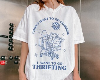 May include: White t-shirt with a blue graphic that reads "I DON'T WANT TO GO CLUBBING, I WANT TO GO THRIFTING." The graphic features a shopping cart filled with various items, a disco ball, and stars.