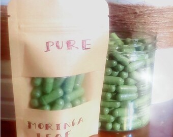 May include: A clear plastic jar filled with green capsules labeled "PURE MORINGA LEAF" and a brown pouch with the same label.