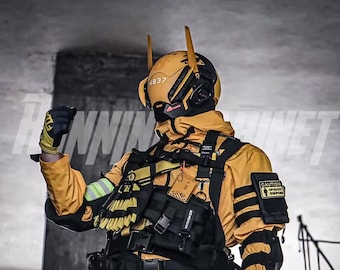 Op de afbeelding: Een persoon die een geel en zwart tactisch pak draagt met een zwarte helm en een zwarte en gele handschoen. De helm heeft een zwart vizier en de tekst "4837" aan de zijkant. De persoon draagt een zwarte riem met een zwarte en gele tas eraan. De persoon draagt ook een zwarte en gele rugzak. De persoon staat voor een grijze muur met een zwart metalen hekwerk op de achtergrond. De persoon houdt een zwarte en gele handschoen in zijn rechterhand. De persoon kijkt naar rechts. De persoon draagt een zwarte en gele handschoen aan zijn linkerhand. De persoon draagt een zwarte en gele rugzak op zijn rug. De persoon draagt een zwarte en gele riem met een zwarte en gele tas eraan. De persoon draagt een zwarte en gele helm met een zwart vizier. De persoon draagt een geel en zwart tactisch pak. De persoon staat voor een grijze muur met een zwart metalen hekwerk op de achtergrond.