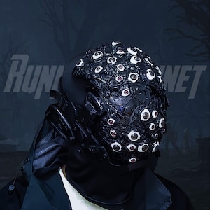 May include: A person wearing a black hooded jacket and a helmet covered in dozens of realistic-looking eyeballs. The helmet is made of a dark, textured material and has a black visor. The person is standing in front of a dark, blurry background.
