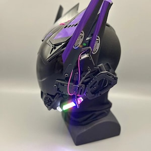 Op de afbeelding: Een zwarte helm met paarse accenten en een verlichtingsfunctie. De helm heeft een futuristisch ontwerp en staat op een zwarte standaard.
