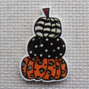May include: A stacked pumpkin decoration with three sections. The top pumpkin is black and white striped, the middle is black with white polka dots, and the bottom is orange with a leopard print design. The stem is brown.