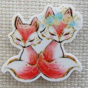 May include: Two red foxes with gold glitter accents are cuddling. The fox on the right has a flower crown with blue and white flowers.