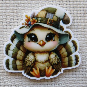 May include: A sticker featuring a cartoon turkey wearing a patchwork hat with a buckle. The turkey has large, expressive eyes, a pink blush, and orange feet. Its feathers are brown and white, and it is decorated with flowers.