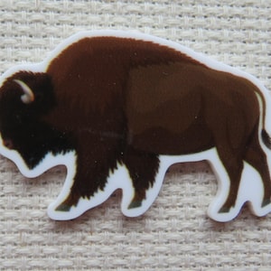 May include: A brown bison sticker with a white border. The bison is depicted in a side profile, with detailed fur and a prominent hump. The sticker is designed to be applied to various surfaces.