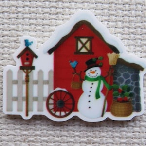 May include: A Christmas-themed sticker featuring a red barn with a snowman, birdhouse, and wagon wheel. The snowman wears a black hat, green scarf, and holds a broom and basket. A blue bird sits on the birdhouse and barn.