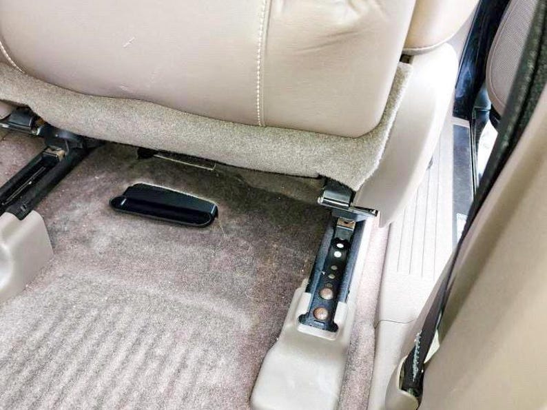 Puede incluir: Primer plano del interior de un coche que muestra la alfombra gris y la hebilla del cintur&oacute;n de seguridad negro. El asiento est&aacute; plegado y el cintur&oacute;n de seguridad est&aacute; asegurado.