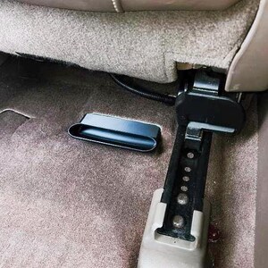 Puede incluir: Un compartimento de almacenamiento de pl&aacute;stico negro est&aacute; unido a la parte posterior de un asiento de coche. El compartimento est&aacute; abierto y parece estar vac&iacute;o.