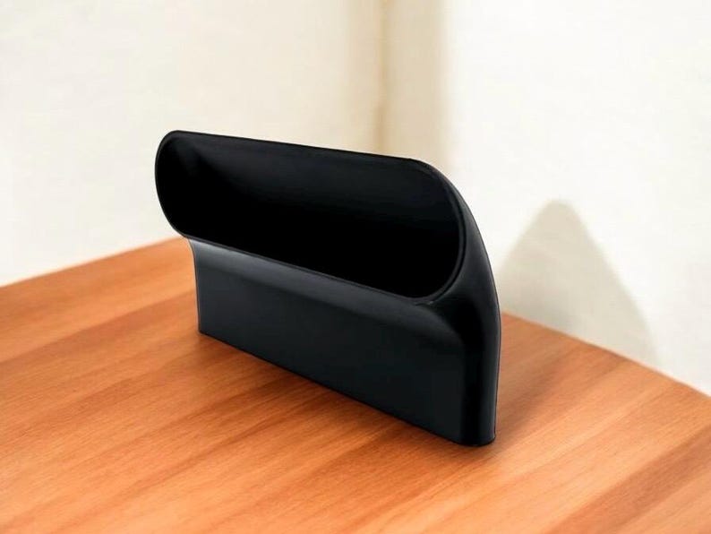 Puede incluir: Un organizador de pl&aacute;stico negro con forma curva y un solo compartimento. El organizador est&aacute; dise&ntilde;ado para guardar objetos como bol&iacute;grafos, l&aacute;pices u otros objetos peque&ntilde;os.