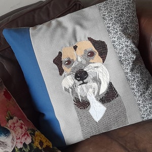 May include: A gray and white patterned throw pillow with a blue border features an embroidered image of a brown and white dog with a white beard.