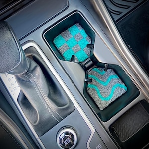 May include: Two gray and turquoise car cup holders with a textured design. The cup holders are in a car's center console.