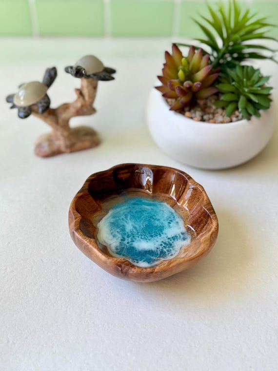 Hibiscus-shaped wooden dish with actual ocean resin poured inside — coastal art and jewelry holder fused into one genuinely striking object.