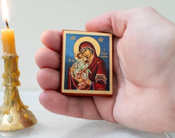 May include: A small wooden icon depicting the Virgin Mary holding baby Jesus. The icon has a gold frame and is painted in vibrant colors. The background is blue with a gold halo around the Virgin Mary's head. The text on the icon reads "A Theotokos".