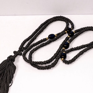 Può includere: Una collana di corda nera annodata con un fiocco e perline blu scuro.