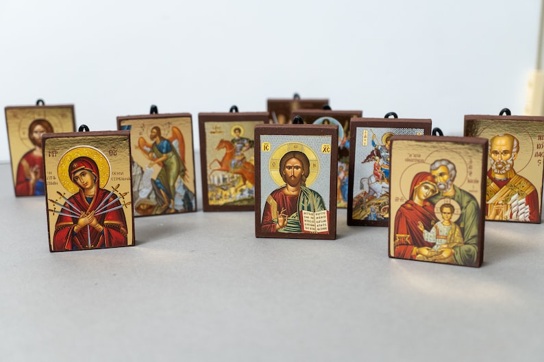 Pode incluir: Uma cole&ccedil;&atilde;o de 10 pequenos &iacute;cones religiosos emoldurados com v&aacute;rias imagens de santos e figuras religiosas. Os &iacute;cones s&atilde;o pintados em um estilo tradicional com detalhes dourados e s&atilde;o exibidos em uma superf&iacute;cie branca.