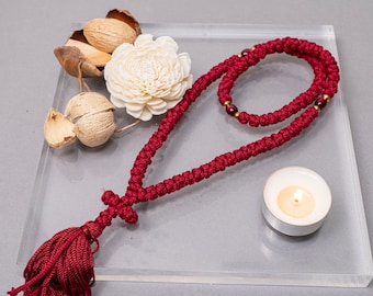 May include: A red prayer rope with a tassel and a cross charm, a small white candle, and dried flowers on a clear glass surface.