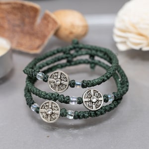 Può includere: Tre corde di preghiera verdi con perline e ciondoli argentati. Ogni ciondolo ha una croce e la scritta "NIKA" incisa su di esso.