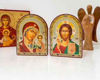 Könnte beinhalten: Zwei kleine, gerahmte religiöse Ikonen aus Holz. Die linke Ikone zeigt die Jungfrau Maria, die das Jesuskind hält. Die rechte Ikone zeigt Jesus, der ein Buch hält. Beide Ikonen haben goldene Verzierungen und sind mit aufwendigen Details verziert.