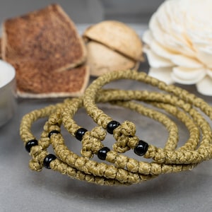 Puede incluir: Un conjunto de tres cuerdas de oración verdes con cuentas negras. Las cuerdas están anudadas y tienen un diseño de cruz.