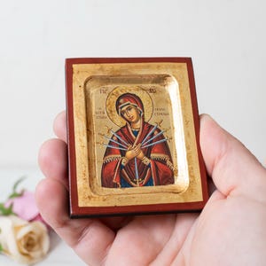 May include: A small, wooden framed icon depicting the Virgin Mary with seven swords piercing her heart. The icon is painted in a traditional style with gold accents and the text "ΠΑΝΤΑ ΥΠΕΡ ΤΗΣ ΕΛΠΙΔΟΣ" in Greek.