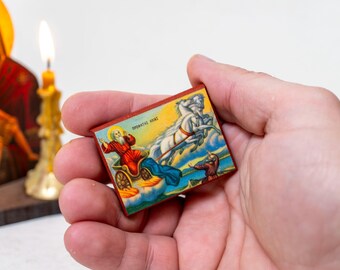 May include: A small wooden icon with a colorful image of a man riding in a chariot pulled by two white horses. The icon has the text "ΘΡΟΝΟΣ ΘΕΟΥ" written on it.