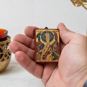 Pode incluir: Um pequeno &iacute;cone de madeira que representa a Ascens&atilde;o de Jesus Cristo. O &iacute;cone &eacute; pintado em cores vibrantes e tem um fundo dourado. O &iacute;cone &eacute; segurado na m&atilde;o.