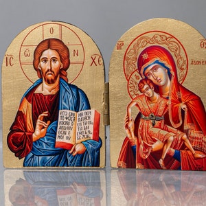 May include: A wooden diptych icon with gold accents. The left panel depicts Jesus holding a book with Greek text. The right panel depicts the Virgin Mary holding the baby Jesus. The text on the right panel reads "09 AZONES".