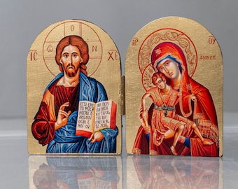 Pode incluir: Um ícone de madeira de duas folhas com detalhes dourados. O painel esquerdo representa Jesus segurando um livro com texto grego. O painel direito representa a Virgem Maria segurando o menino Jesus. O texto no painel direito diz "09 AZONES".