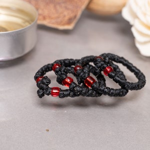 May include: Four black prayer ropes with red beads, stacked on a gray surface.