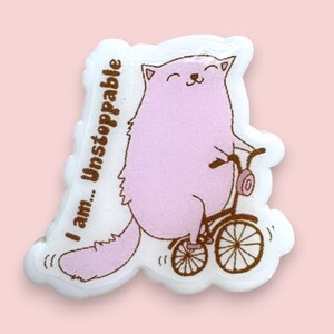 May include: A pink cat riding a tricycle with the text "I am... Unstoppable" on the side. The cat is smiling and has a pink tail.