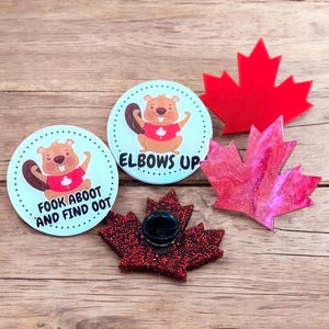 May include: Three Canadian themed pins featuring a beaver with the text "Fook Aboot And Find Oot", a beaver with the text "Elbows Up", and a red glitter maple leaf.
