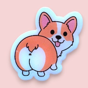 May include: A white sticker featuring a cartoon image of a corgi dog's rear end. The corgi is orange and white with a black tail and black eyes. The corgi is looking back over its shoulder with its tongue sticking out.