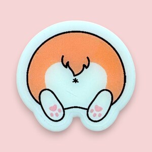 May include: A light blue sticker featuring a cartoon image of a dog's rear end. The dog is orange and white with a black tail and black eyes. The dog is sitting with its legs tucked under its body. The sticker has a pink paw print on each of the dog's hind legs.
