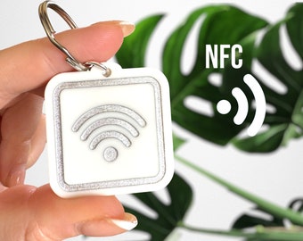 May include: White square keychain with a silver Wi-Fi symbol and the word "NFC" on a green leafy background.