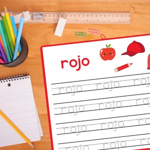 Pode incluir: Uma ma&ccedil;&atilde; vermelha com um rosto feliz, um bon&eacute; de beisebol vermelho, um su&eacute;ter vermelho e um l&aacute;pis vermelho s&atilde;o mostrados em uma folha de papel branca com a palavra "rojo" escrita em letras grandes no topo. A palavra "rojo" est&aacute; escrita em cursiva em cinco linhas com linhas pontilhadas para ajudar a guiar a escrita.