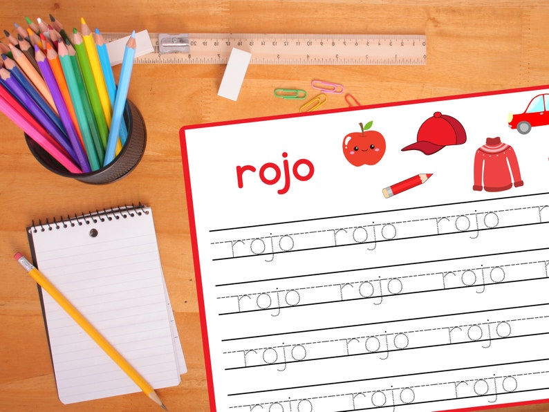 Pode incluir: Uma ma&ccedil;&atilde; vermelha com um rosto feliz, um bon&eacute; de beisebol vermelho, um su&eacute;ter vermelho e um l&aacute;pis vermelho s&atilde;o mostrados em uma folha de papel branca com a palavra "rojo" escrita em letras grandes no topo. A palavra "rojo" est&aacute; escrita em cursiva em cinco linhas com linhas pontilhadas para ajudar a guiar a escrita.