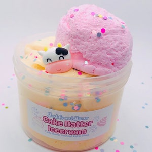 Pode incluir: Um recipiente de plástico transparente cheio de slime amarelo e rosa, coberto com uma bola de slime rosa e uma figura de vaca. O recipiente tem um rótulo que diz "Cake Batter Icecream". Confetes coloridos estão espalhados ao redor do recipiente.