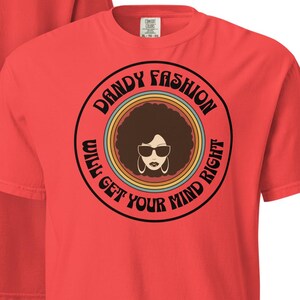 Può includere: Maglietta rossa con una grafica retrò di una donna con un afro che indossa occhiali da sole e il testo "Dandy Fashion Will Get Your Mind Right".