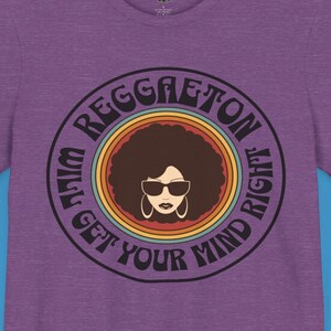 以下が含まれることがあります： 紫色のTシャツに、サングラスをかけた女性のレトロなグラフィックと「I'm Reggaeton, Will Get Your Mind Right」というテキストがプリントされています。