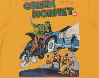 Può includere: Una maglietta gialla con una copertina di fumetto vintage che presenta il Green Hornet. La copertina è illustrata con il Green Hornet in un'auto blu, che si allontana da un uomo con una pistola. Il testo sulla copertina recita "Green Hornet" e "December 10c".