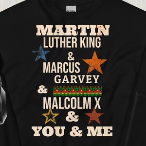 Può includere: Felpa nera con una grafica in stile vintage che presenta i nomi di Martin Luther King, Marcus Garvey, Malcolm X e la frase "You & Me".