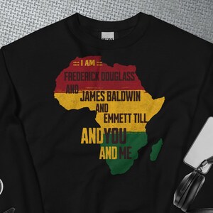 Può includere: Felpa nera con una grafica del continente africano in rosso, giallo e verde. La grafica include il testo "Io sono Frederick Douglass e James Baldwin e Emmett Till e tu e io."