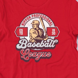 Puede incluir: Camiseta roja con un logotipo vintage de liga de béisbol que presenta a un jugador sosteniendo un bate. El logotipo dice "Nippon Professional Baseball League" con los años "1930" y "65 a 70" en los lados.